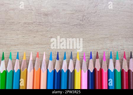 Viele mehrfarbige helle Bleistifte in einer geraden Reihe auf einem Holzhintergrund Stockfoto