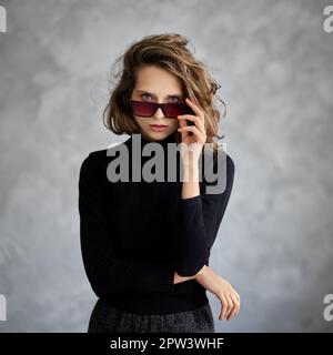 Das lockige Mädchen sieht gerade aus, wenn es eine Sonnenbrille hinlegt. Stockfoto