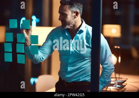 Und schließlich kam der Plan zusammen. Ein erwachsener Geschäftsmann, der abends in einem modernen Büro ein Brainstorming durchführt. Stockfoto