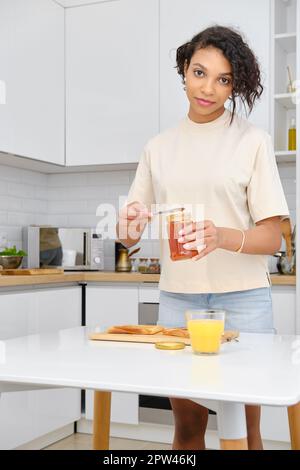 afroamerikanischer Waamn hält Aprikosenmarmelade in der Hand. Sie wird süßen Toast machen. Stockfoto