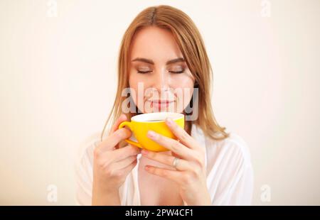 Erwachsene Frau in Robe, die die Augen schließt, während sie eine Tasse davon hat Aromatischer, frisch gebrühter schwarzer Kaffee Stockfoto