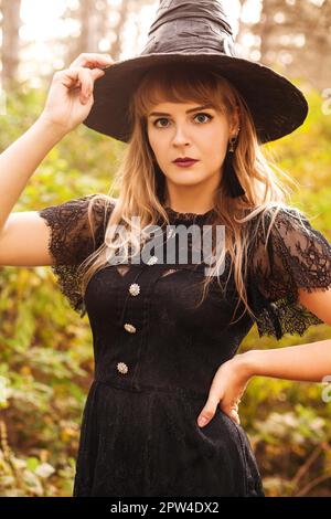 Junge Frau in schwarzem Umhang mit gruseligen Jack o Laterne Und auf den Halloween-Tag im Herbstwald wegschauen Stockfoto