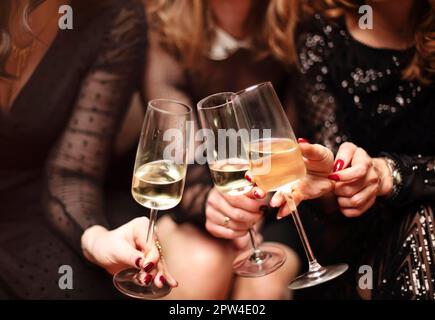 Unkenntliche Freundinnen in eleganten Kleidern klirren Gläser Champagner und schlagen Toast während der Party Stockfoto