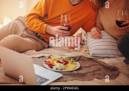 Junger Mann und Frau umarmen und genießen Rotwein während romantischen Date zu Hause Stockfoto