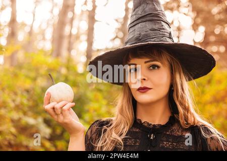 Junge Frau in schwarzem Umhang mit gruseligen Jack o Laterne Und auf den Halloween-Tag im Herbstwald wegschauen Stockfoto