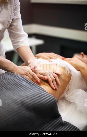 Teilansicht des Masseurs, der auf dem Massagetisch eine Magenmassage für die Frau macht Stockfoto