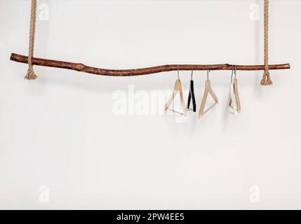 Set mit fünf leeren Kleiderbügeln, die an einem rustikalen Holzstab an einem dicken Seil hängen, isoliert über weißen Studiowandhintergrund mit Kopierplatz für Stockfoto