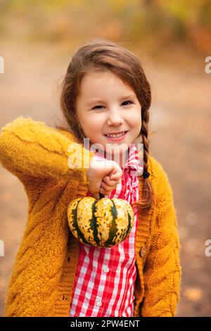 Kleine Hündin im lässigen karierten Hemd mit orangefarbenem Mini-Kürbis in den Händen Stockfoto