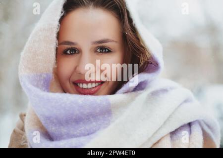 Nahaufnahme einer hübschen braunen Frau mit scharfem Look, die Hälfte der jungen Frau mit einem hellen Strickschal bedeckt, ein Mädchen schaut hinein Stockfoto