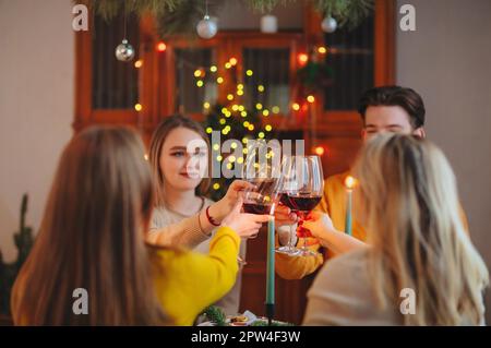 Glückliche junge Freunde klirren Gläser Wein über Tisch für Weihnachtsfeier zu Hause dekoriert Stockfoto