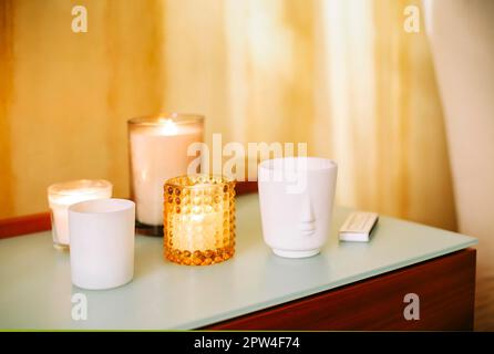Tisch mit vielen brennenden Duftkerzen und aromatischen Räucherstäbchen im Spa-Massagesalon oder Yoga-Studio, selektiver Fokus. Meditationsort Stockfoto