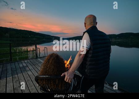 Niedliches Paar beobachtet den Sonnenuntergang am Kamin auf dem Pier (Blick von hinten) Stockfoto