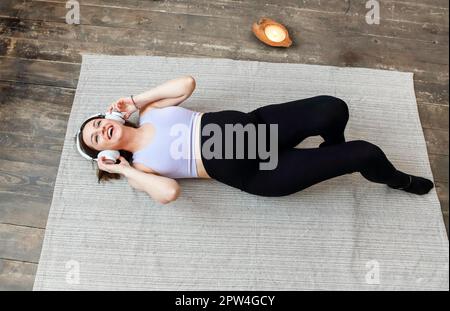 Bild einer erstaunlichen gesunden Schwangeren zuhause auf dem Boden auf dem Sofa, die Musik mit Kopfhörern hört. Happy Pregnacy Konzept Stockfoto