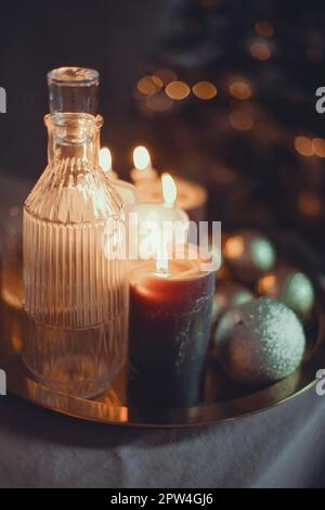 Silvester-Stillleben. Gläser und eine Karaffe aus transparentem Glas, Kerzen und goldene Weihnachtsbällchen. Festliches Festmahl. Der Tisch ist mit einem Schwarzen gedeckt Stockfoto