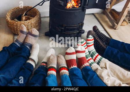 Verkürztes Foto einer großen Familie, die im Winter warme Wollsocken trägt und am Kamin ruht. Mutter, Vater und Kinder liegen auf dem Boden Stockfoto
