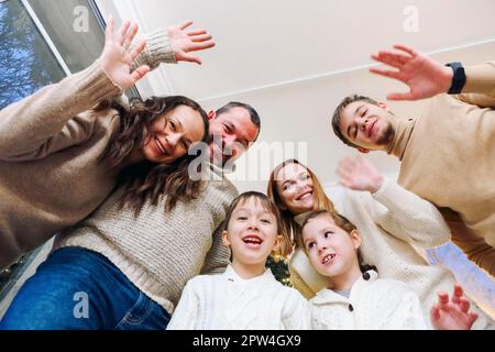 Blick von unten auf eine glückliche, große, weiße Familie mit vielen Kindern, die zu Hause Selfie-Fotos machen, Eltern mit Kindern, die vor der Kamera mit den Händen winken und haben Stockfoto