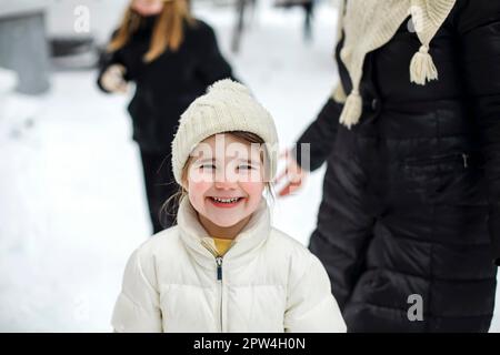 Fröhliche Familiengroßmutter mit Enkelkindern in warmen Kleidern, die im Winterpark im Freien spielen, frostiges und verschneites Wetter genießen, Kinder aktiv Stockfoto