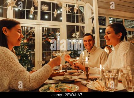 Glückliches Familienpaar, das mit Freunden Silvester oder Weihnachten mit Champagnergläsern feiert und mit dem man am festlichen Esstisch sitzt Stockfoto