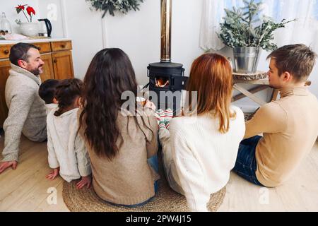 Verkürztes Foto einer großen Familie, die im Winter warme Wollsocken trägt und am Kamin ruht. Mutter, Vater und Kinder liegen auf dem Boden Stockfoto