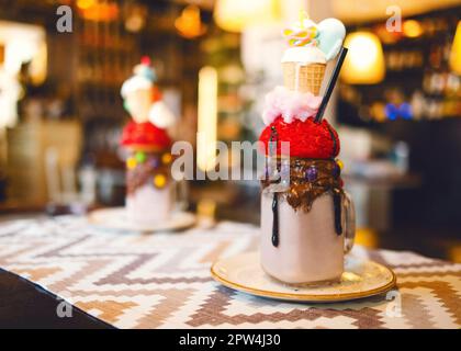 Schokoladenmilchshake mit Eis und Schlagsahne, Marshmallows, süße Kekse, Waffeln, serviert in einem Glasmauerwerk. Freak oder verrückter süßer Cocktail Stockfoto
