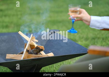 Feuerholz im Grill im Freien und entkochte Hand mit einem Glas Limonade auf dem Hintergrund Stockfoto