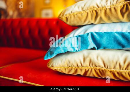 Orange-, Blau- und Beige-Kissen auf einem bequemen roten Sofa in einem schicken Wohnzimmer. Schließen Stockfoto