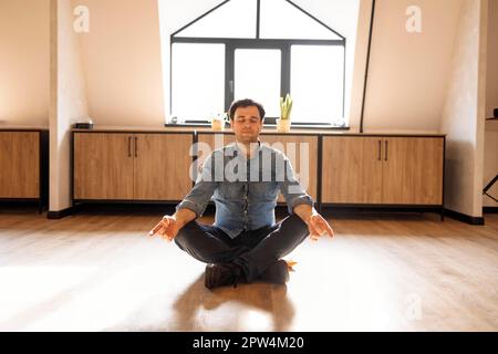 Gutaussehender hispanischer Mann trägt Jeans Casual Shirt sitzt auf dem Boden zu Hause entspannen, Meditation Geste mit den Fingern zu tun. Yoga-Konzept Stockfoto