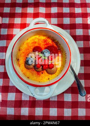 Creme Brulee, verbrannte Sahne. Süßes gebackenes Dessert auf einem weißen Porzellanteller mit Griffen. Gericht, dekoriert mit Johannisbeeren und Blaubeeren. Platte und Stockfoto