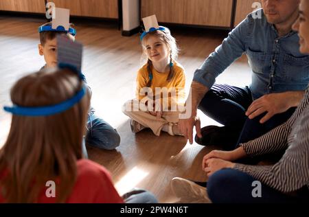 Glückliche junge Familie mit Kindern, die zu Hause ein Kartenspiel spielen und auf dem Boden sitzen. Mutter, Vater, Sohn und Töchter spielen Kartenspiele im Wohnzimmer Stockfoto