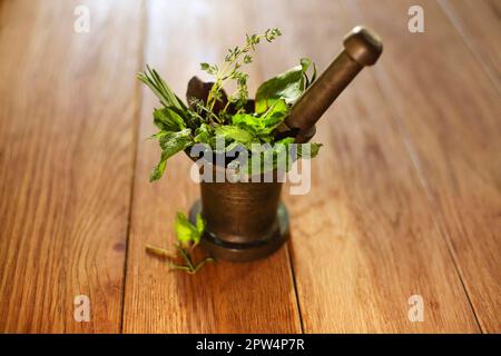 Hoher Winkel von frischen Kräutern und Stößel in Bronze platziert Mörtel auf dem Tisch isoliert Stockfoto