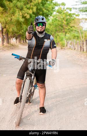 Radfahrer, der auf der Straße Daumen nach oben zeigt. Professioneller Radfahrer, der eine gute Geste auf seinem Fahrrad macht Stockfoto