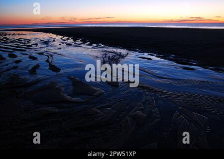 Der helle Sonnenhimmel spiegelt sich in den Wellen und Sandleisten des Strandes und der Küste am Meeresrand wider Stockfoto