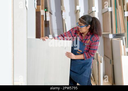 Eine Frau mittleren Alters, die Sperrholz aus einem Lagerfach zieht. Asiatischer Zimmermann arbeitet in einer Möbelfabrik. Stockfoto