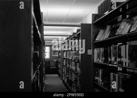 Eine Insel mit Bücherregalen auf beiden Seiten in der Lucius Beebe Memorial Library. Wakefield, Massachusetts. Das Bild wurde mit analogem Schwarz und Weiß aufgenommen Stockfoto