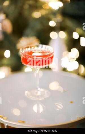 Vertikale Aufnahme klassischer kosmopolitischer Cocktails aus Glas, die auf dem Tisch im Nachtclub oder Restaurant stehen, bei verschwommenen festlichen Lichtern und Glitzern. Stockfoto