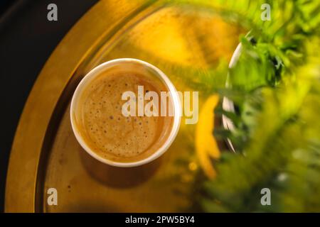 Blick von oben auf die Kaffeetasse auf dem Kaffeetisch mit grüner Topfpflanze, selektiver Fokus. Aromatischer Duft frisch gebrühter Cappuccino oder Latte mit Schaum Stockfoto