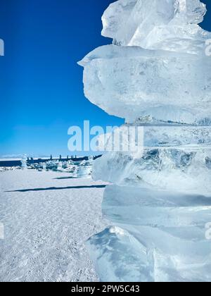 Eisstücke liegen auf dem idealen glatten Eis von baikal mit Eishummocks am Horizont. Die Sonne scheint durch die Seiten der Eiswürfel. Schollen-Look Stockfoto