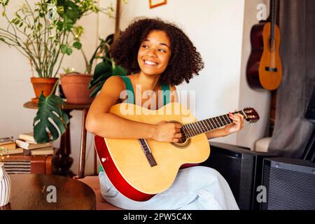 Lächelnde afro amerikanische junge Frau, die akustische Gitarre spielt. Mädchen spielt Gitarre Stockfoto