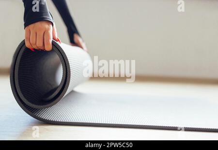 Seitenansicht einer anonymen dünnen Abrollmatte für Yoga-Übungen im weißen Studio Stockfoto