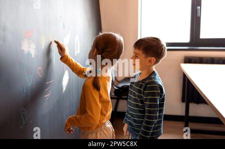 Süßes kleines Mädchen und Junge, gemalt mit Buntstift an der Wand. Kinderwerke. Süße Geschwister, die auf eine Tafel schreiben Stockfoto