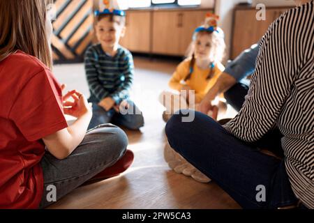 Glückliche junge Familie mit Kindern, die zu Hause ein Kartenspiel spielen und auf dem Boden sitzen. Mutter, Vater, Sohn und Töchter spielen Kartenspiele im Wohnzimmer Stockfoto