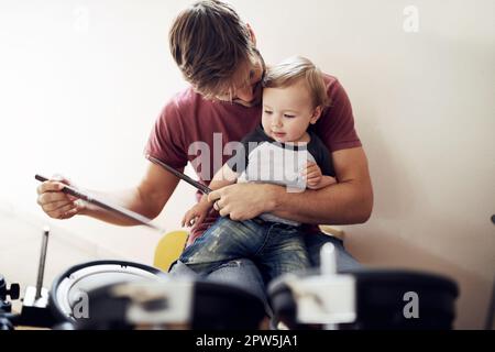 Listen....ca, du hörst es. Ein attraktiver junger Vater, der seinem Sohn das Trommeln beibringt Stockfoto