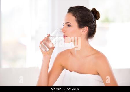 Sie trinkt ihre Haut für einen frischen Look. Seitenansicht einer schönen Frau, die ein Glas Wasser trinkt Stockfoto