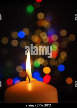 Eine weiße Kerze brennt mit bunten Weihnachtslichtern im Hintergrund, Platz für Text Stockfoto