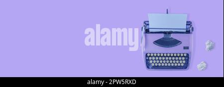 Eine violette Vintage-Schreibmaschine mit violettem Hintergrund und zwei Papierkugeln. Stockfoto