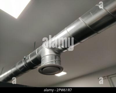 Abzugshaube in einer öffentlichen Toilette. Rundes Metallrohr mit grauem Luftabsauger. Technische Lüftungssysteme. Verzinkte Rohre unter der Decke von Th Stockfoto