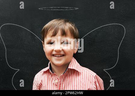 Zeichnen macht so viel Spaß. Studiofoto eines niedlichen kleinen Jungen mit Kreidezeichnungen hinter ihm Stockfoto