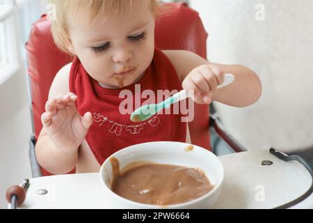 Der wachsende Junge braucht sein Essen. Ein kleiner Junge, der in seinem Hochstuhl nach Herzenslust isst Stockfoto