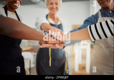 Eine Gruppe von Bekleidungsdesignern, die ihre Hände bei der Arbeit in einem Geschäft zusammenstapeln. Schneiderinnen, die Spaß beim Stehen haben und ihre Hände für Unterstützung und Einheit stapeln Stockfoto