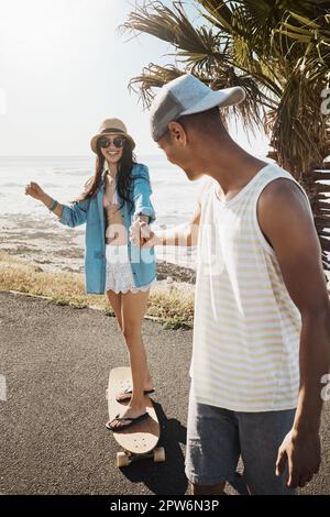 Ich will skaten, bis die Sonne untergeht. Ein junger Mann brachte seiner Freundin Skateboard auf der Promenade bei. Stockfoto